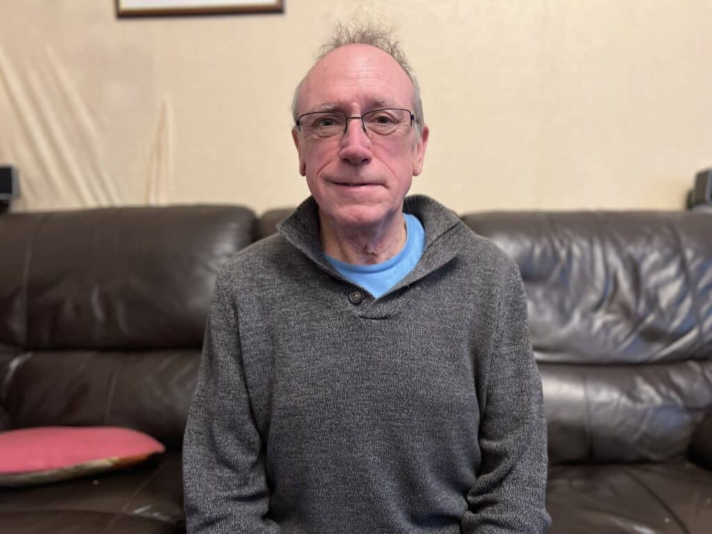 A photo of a 62-year-old man sitting on a sofa in his living room.