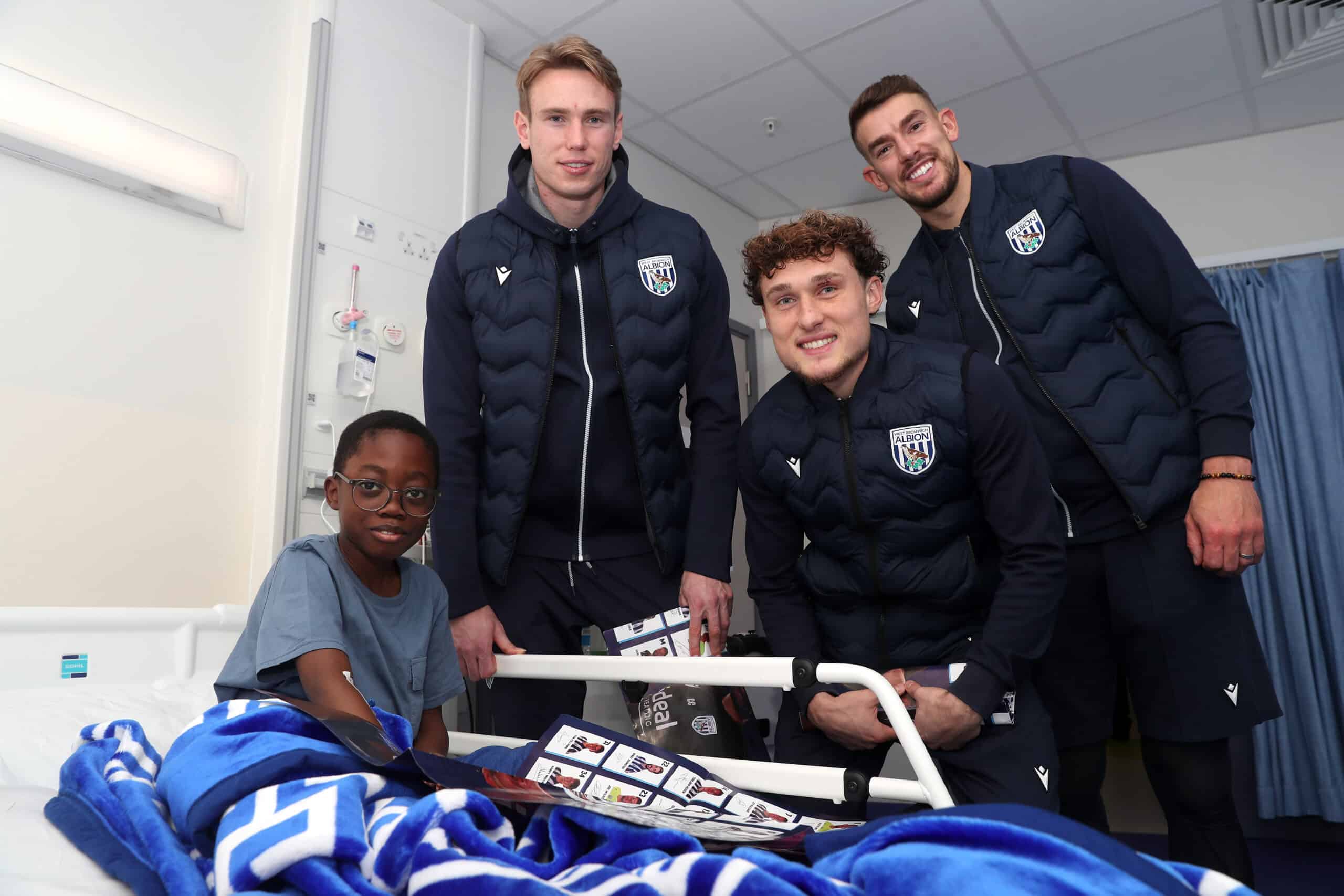 A child in a hospital ward with football players who are giving out Christmas gifts