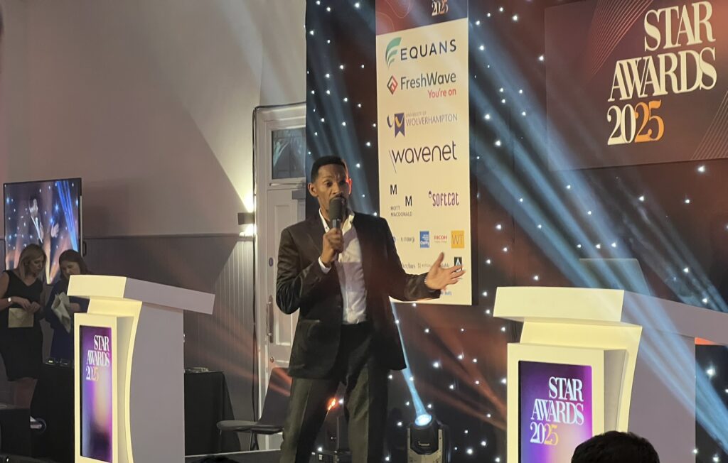 Des Coleman, ITC Central weatherman, standing on stage and presenting at a black tie event